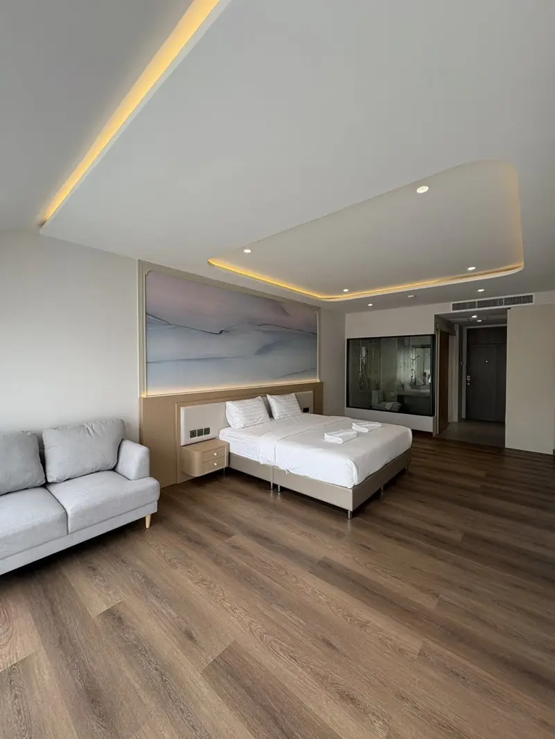 Bed and grey sofa on a wooden floor, with a glass-walled bathroom behind