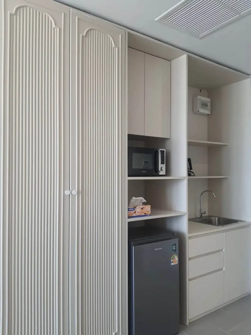 White wardrobe with fluted doors next to a kitchenette with a small sink, shelves, a microwave and a small fridge