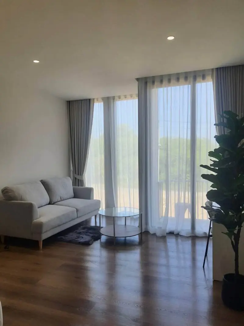 Sitting area with a grey sofa, a round glass table and a plant beside tall curtained windows